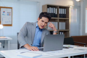 Stressed asian businessman looking worriedly at laptop in office