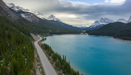 Obraz premium Snowy mountain range, winding road, and turquoise lake. A scenic drive through the Canadian Rockies. Waterfowl Lake, Banff National Park, Alberta, Canada