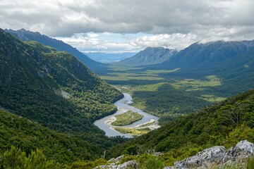 Fototapeta premium Scenic aerial view of a winding river through lush green valleys and mountains under a cloudy sky