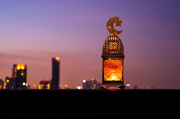 Golden lantern that have moon symbol on top with dusk sky and city background for the Muslim feast of the holy month of Ramadan Kareem.