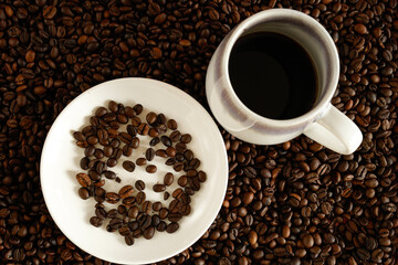 Black coffee on a bed of coffee beans, with coffee beans in a white saucer beside it.