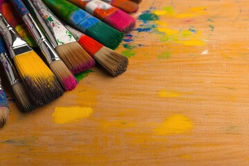 Fototapeta premium close-up of colorful paints and brushes scattered across wooden table during school art workshop vibrant paint strokes