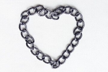 A metal chain in the shape of a heart on a white background. The concept of psychological limitations, the desire to overcome depression, the offer of obstacles. Work on childhood injuries.