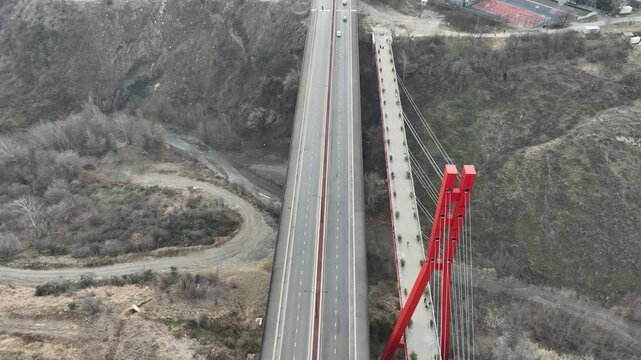 A red bridge spans a narrow gorge, combining modern engineering with natural features. The aerial perspective captures the interplay between human-made structure and rugged terrain