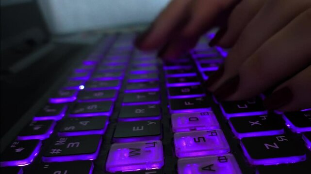 Female hands are typing on a purple-backlit keyboard. The concept of new technologies, hacker attacks, online computer games, online fraud. The flow of information.