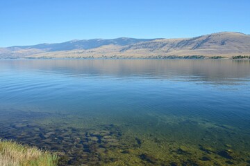 Fototapeta premium Mountain Lake Gradient: A mountain lake with water transitioning from clear near the shore to deep blue in the center.