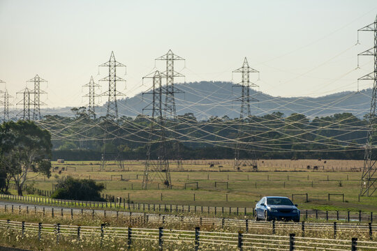 Electrical transmission towers along an Australian country road with a rural landscape, rolling hills and farmland-Expansive field beneath the power lines of energy infrastructure on agricultural land