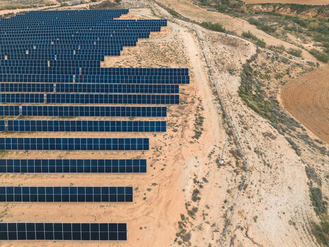 A vast array of solar panels stretches across a desert terrain, emphasizing sustainable energy solutions in the backdrop of nature's raw beauty in Zaragoza Spain