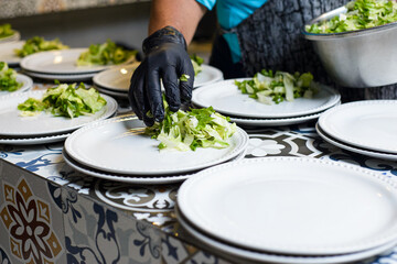 A chef in black gloves meticulously places fresh, chopped lettuce onto white plates