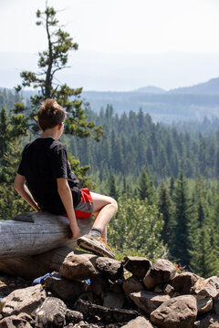 Youth boy sitting on log overlooking horizon and scenic treed valley