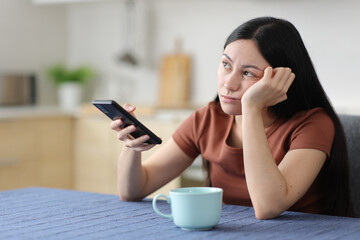Bored asian woman holding smart phone in the kitchen