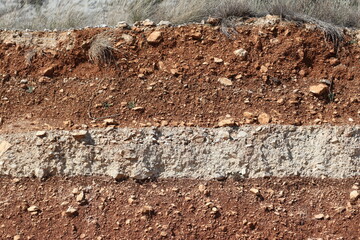 Brown and cream-colored sediment layers along a roadside on the mountain slopes