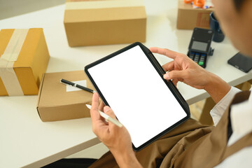 Small business owner managing orders on digital tablet and preparing packages for shipment