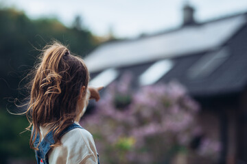 Young girl looking at house with solar panels on roof, standing outdoors in garden.