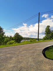 Scenic Rural Road with Gravel Surface, Utility Poles, and Lush Greenery Under a Bright Blue Sky – Tranquil Countryside Landscape with Natural Beauty