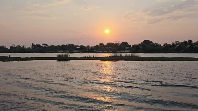 Golden sunset reflecting on the calm waters of the chobe river, with tourist lodges along the riverbank in chobe national park