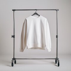 A photograph of a plain white crewneck sweatshirt hanging on a metal clothing rack, set in a minimal studio