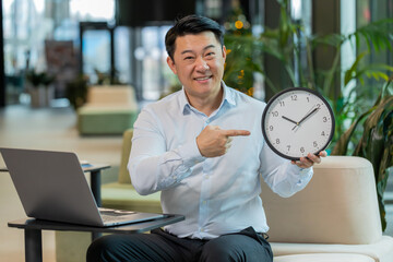 It is your time. Mature boss businessman with laptop showing time on wall clock, approve, pointing...