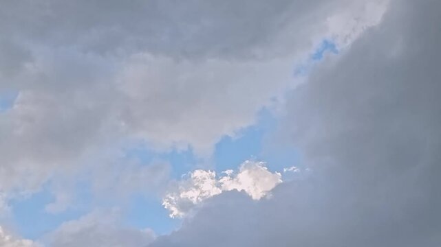 Timelapse white and silver clouds move across the sky in an abstract manner with sunlight shining through the clouds in the morning