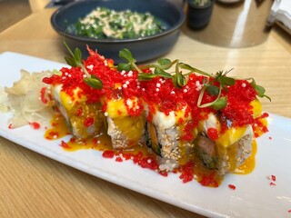 Close up Japanese restaurant table with Red Dragon Sushi, seaweed salad. Sushi with salmon, panko tiger prawns, cucumber, unagi sauce, mayonnaise, sesame seeds
