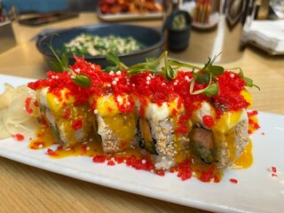 Close up Japanese restaurant table with Red Dragon Sushi, seaweed salad. Sushi with salmon, panko tiger prawns, cucumber, unagi sauce, mayonnaise, sesame seeds