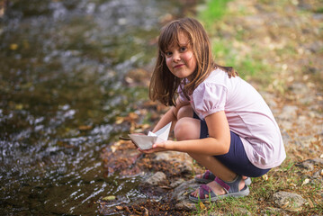 Young girl launching paper boat into stream in nature