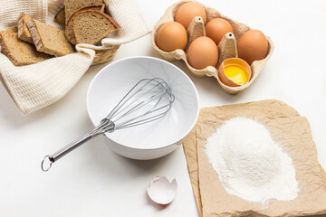 Whisk in bowl. Flour on paper. Eggs in cardboard container