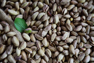 Pistachio nut in sack bag with mint green leaf on wooden table background.