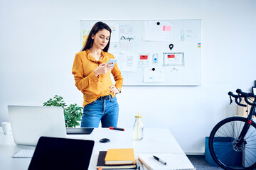 Businesswoman holding smartphone at whiteboard in office