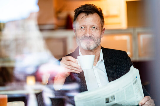 Portrait of smiling mature businessman with newspaper in a coffee shop drinking coffee