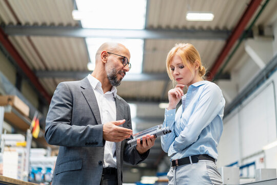 Businessman and businesswoman examining workpiece in factory