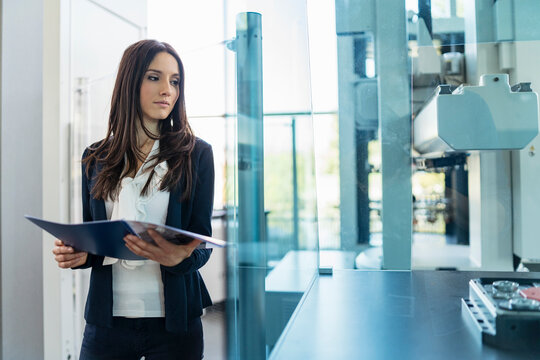 Businesswoman holding folder looking at a machine in modern factory