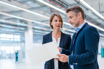 Businessman and businesswoman discussing plan in a factory hall