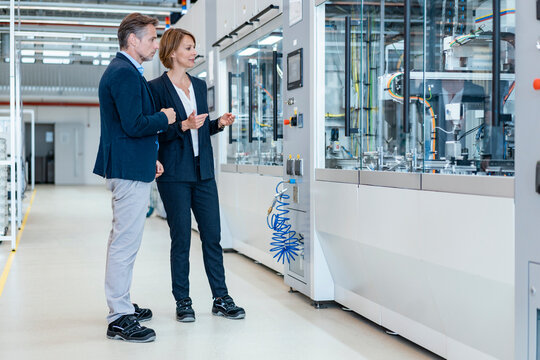 Businessman and businesswoman looking at a machine in a modern factory hall