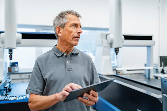 Engineer holding tablet PC near machine at factory