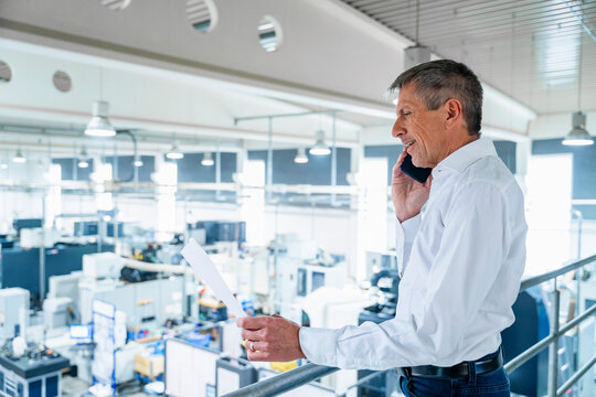 Businessman holding document and talking on smart phone at factory