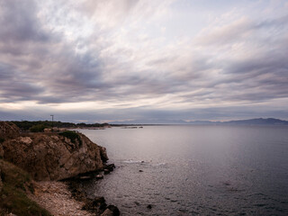 rocky shoreline with a cloudy sky and a calm ocean with deep blue water, concept of peaceful and serene seascape, copyspace for text