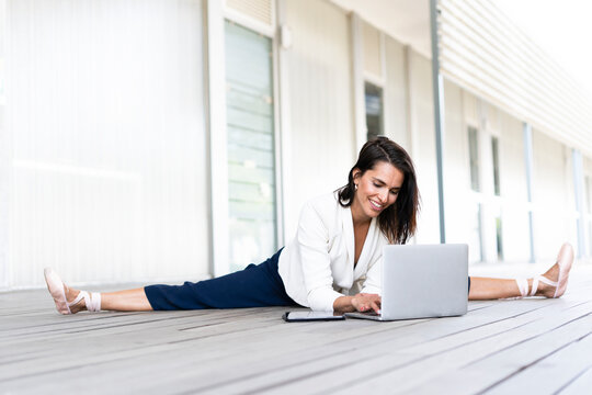 Female balett dancer sitting on the ground, using tablet and laptop