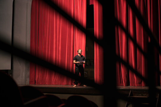 Barefoot actor with script standing on theatre stage