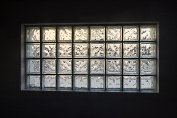 Light filters through a textured glass block window, creating a unique visual effect in a darkened room during early morning hours