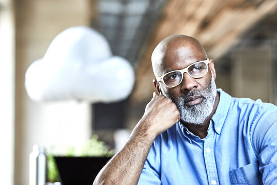 Mature businessman in office thinking with cloud balloon in background