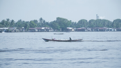 Obraz premium Local Motorboat Navigating the Barito River with Residents in Lush Setting on a Sunny Day in Indonesia