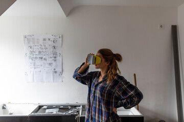 Young woman wearing VR glasses with assembly instructions at kitchen wall