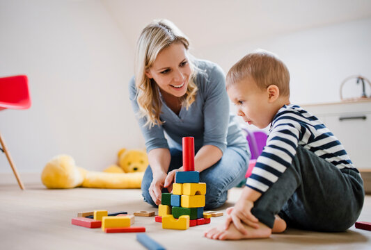 Happy mother and toddler son playing with building blocks at home