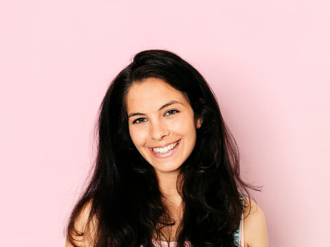 Portrait of young smiling woman with black hair in front of pink background