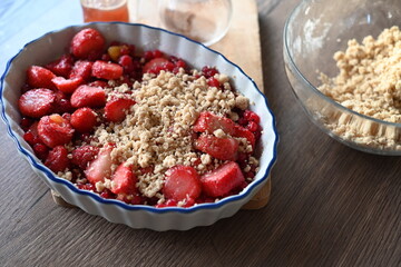 Close-up view of a bowl filled with fresh strawberries and red currants, prepared for baking. A delicious homemade fruit crumble