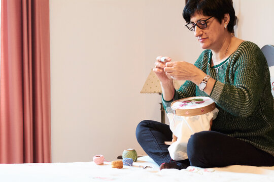 Woman embroidering sitting on bed at home