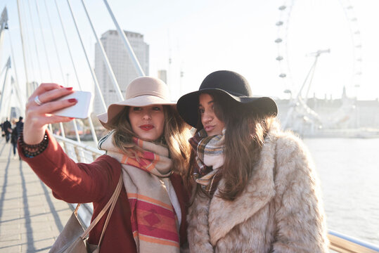 UK, London, two women taking a selfie on Millennium Bridge with London Eye in background