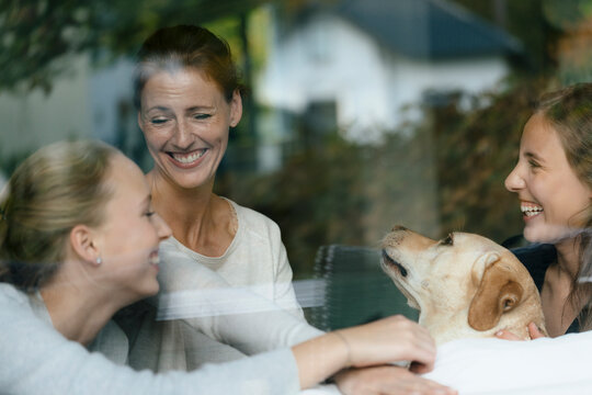 Happy mother with two teenage girls and dog behind windowpane
