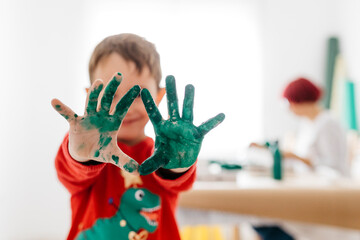 Boy showing his hands painted green while doing crafts at home